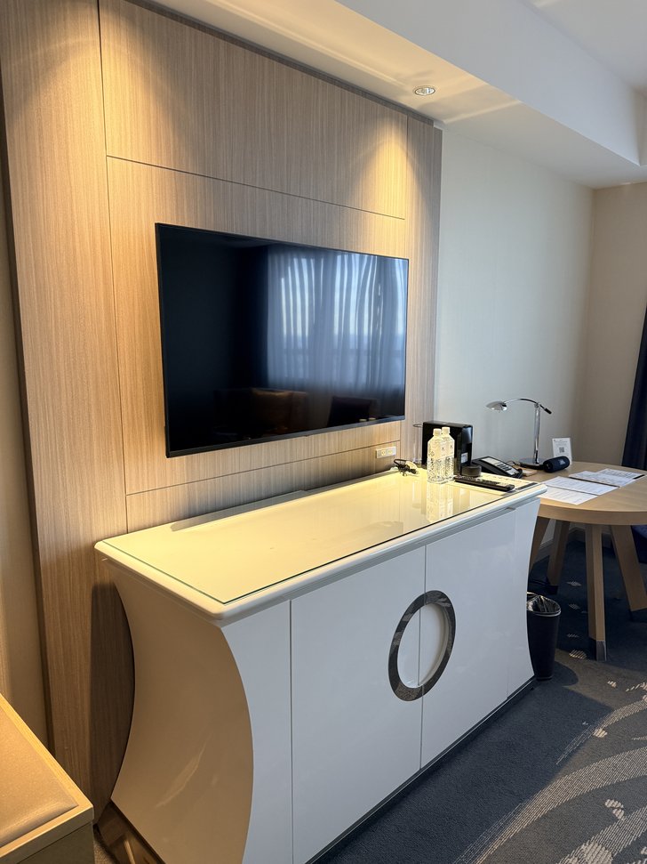 壁掛けテレビと白いキャビネット、丸テーブルのある部屋