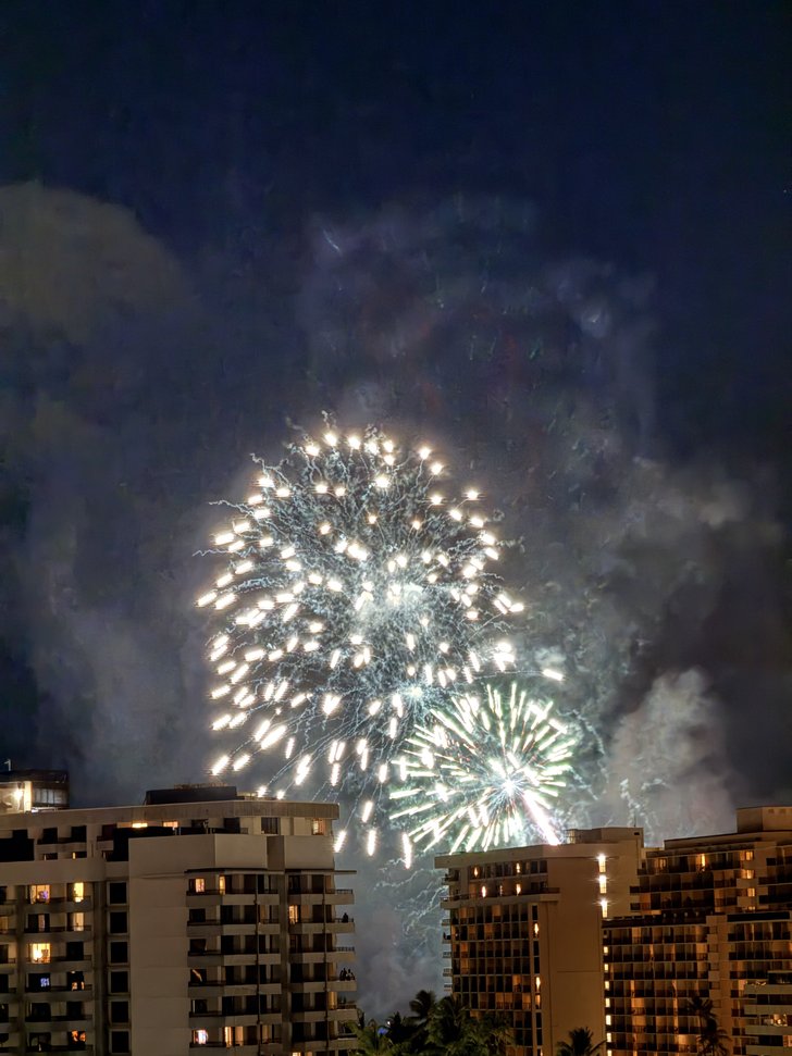 高層建物の上に咲く白と緑の花火